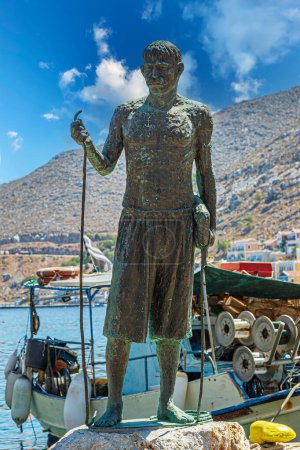 Foto de SYMI, GRECIA - 3 de julio de 2022: Estatua de Stathis G. Hatzis (1878-1936) que fue la cabeza de los buzos esponja en Symi a principios del siglo XX. En 1913, se sumergió a una profundidad de 88 metros, durante 4 minutos. - Imagen libre de derechos