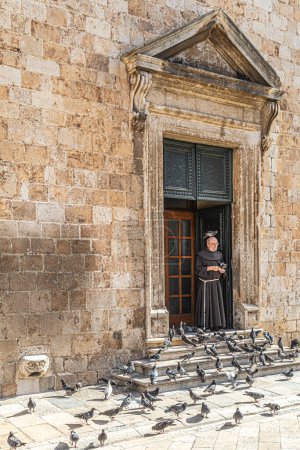 Photo for DUBROVNIK, CROATIA-AUGUST 18, 2022: Funny situations with a monk very friendly feeding the pigeons in front of the Franciscan Monastery and Church (Croatian: Franjevacki samostan i crkva u Dubrovniku) - Royalty Free Image