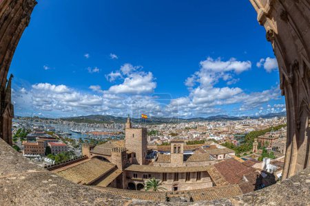 Blick von der Terrasse der mittelalterlichen Kathedrale Santa Maria von Palma auf das Dach des Königspalastes von La Almudaina und den Turm mit der spanischen Flagge. Im Hintergrund der Hafen von Palma, Spanien.