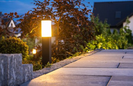 Primer plano de la lámpara de pilona del jardín instalada a lo largo de la pasarela en el jardín del patio trasero ajardinado. Hora de la tarde. Tema de iluminación exterior.