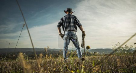 American Caucasian Cowboy en sus 40 años Supervisar su campo Farmland estancia con la cuerda en su mano