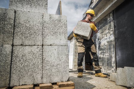 Téléchargez les photos : Travailleur de la construction Déménagement de matériaux de construction dans ses mains. Livraison de blocs de béton denses creux - en image libre de droit