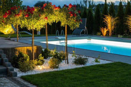 Modern Illuminated Residential Outdoor Swimming Pool, Poolside and the Back Yard. Night Time Scenery.
