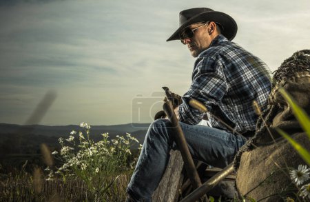 Photo for American Cowboy in His 40s Enjoying Free Time on His Countryside Ranch. Seating on a Piece of Wooden Crate. - Royalty Free Image