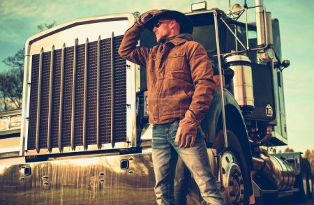 Kaukasischer Texas Cowboy Semi Truck Driver in seinen Vierzigern. Amerikanischer Trucker und sein Schwerlastfahrzeug. Thema Bodenverkehr.