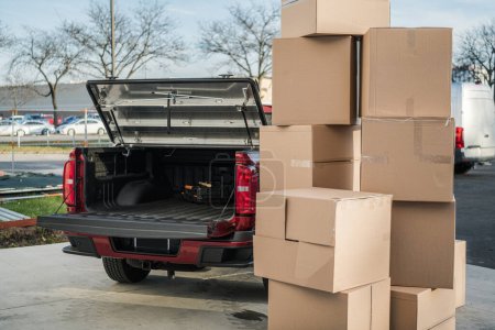 Photo for Stack of Cardboard Packages Placed Outside Ready to Be Loaded for Transportation. Pickup Truck with Open Trunk in the Background. Moving Services Theme. - Royalty Free Image