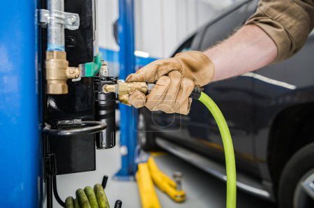 Téléchargez les photos : Gros plan du mécanicien branchant un tuyau sur l'outil de compresseur d'air de roue fixe installé dans l'atelier professionnel de voiture. - en image libre de droit