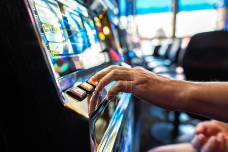 Nahaufnahme des Spielers, der den Drehknopf drückt, während er Spielautomaten im Casino spielt. Thema Glücksspielindustrie.