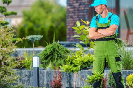 Téléchargez les photos : Professionnel caucasien moyen âge paysagiste jardinier debout au milieu de jardin arrière-cour de son client penser à l'aménagement paysager amélioration de la conception. - en image libre de droit