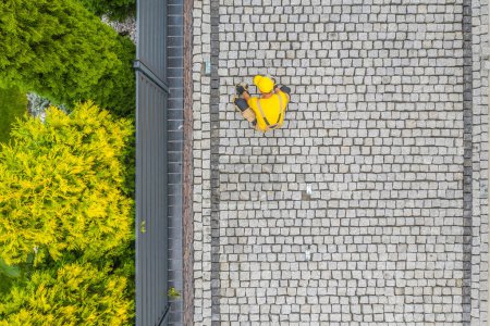 Téléchargez les photos : Aerial View of Contractor Finishing Building of Granite Brick Driveway Along the Fence. Domestic Yard Design and Construction Theme. - en image libre de droit