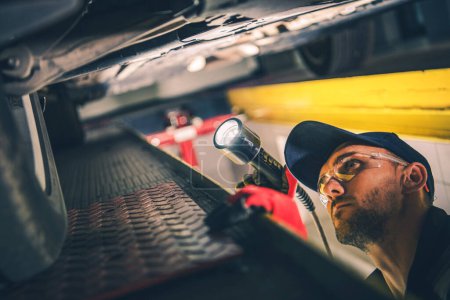 Photo for Professional Mechanic Checking Car Undercarriage with a Flashlight During Scheduled Vehicle Inspection Appointment at Automobile Station. - Royalty Free Image