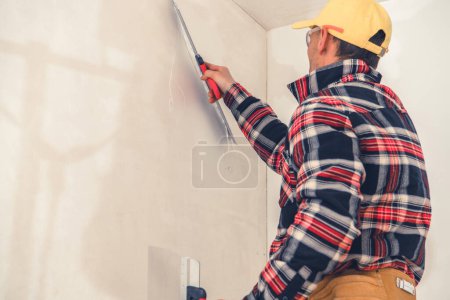 Foto de Professional Caucasian Plasterer in Checkered Shirt Plastering Interior Walls with Putty. House Renovation Work. Construction Theme. - Imagen libre de derechos