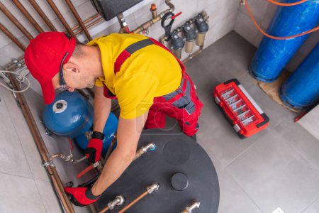 Foto de Professional Plumber Performing Residential Hot Water Heater Check. Heating System Maintenance Theme. Aerial View. - Imagen libre de derechos