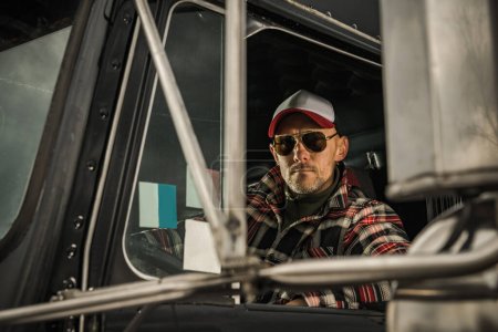 Foto de Professional Semi Truck Driver Behind the Wheel. Caucasian Man in His 40s. Transportation Industry Theme. - Imagen libre de derechos