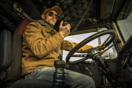 Téléchargez les photos : Ground Transportation Industry Theme. Caucasian Trucker Driver CB Radio Talk Inside a Old Semi Truck - en image libre de droit