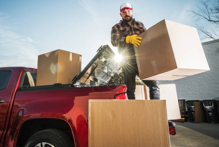 Téléchargez les photos : Caucasian Man Moving Boxes To His New Apartment. Transporting Carton Boxes on a Pickup Truck. - en image libre de droit