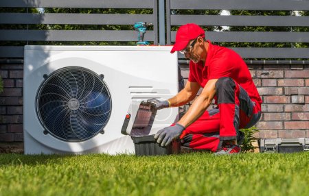 Foto de Professional Caucasian Heat Pumps Technician in His 40s Installing New Residential Modern Heating Device. HVAC Industry Theme. - Imagen libre de derechos