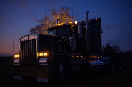 Téléchargez les photos : Industrie des transports. Tracteur semi-camion américain classique dans la lumière du crépuscule scénique. Tous les feux extérieurs du véhicule allumés. - en image libre de droit
