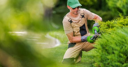 Foto de Contratista de jardinero profesional de 40 años con cizallas de cobertura que realizan mantenimiento del patio trasero de primavera. - Imagen libre de derechos