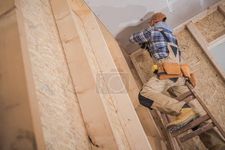 Foto de Professional Contractor Standing on Ladder During Ceiling Installation in Newly Built Residential House. Construction Theme. - Imagen libre de derechos