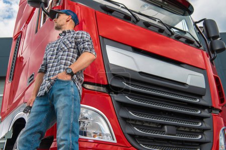 Téléchargez les photos : Camionneur caucasien professionnel Fièrement debout devant son nouveau semi-camion rouge. Thème Transport lourd. - en image libre de droit