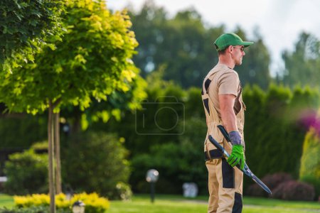 Photo for Smiling Caucasian Gardener with Hedge Shears in His Hand During Pruning and Trimming Work in Residential Backyard Garden. - Royalty Free Image