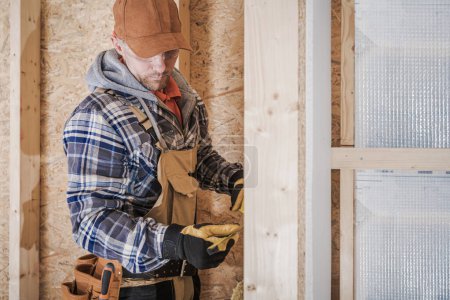 Téléchargez les photos : Caucasian General Construction Worker in His 40s Taking Measurements Inside Newly Developed House. - en image libre de droit