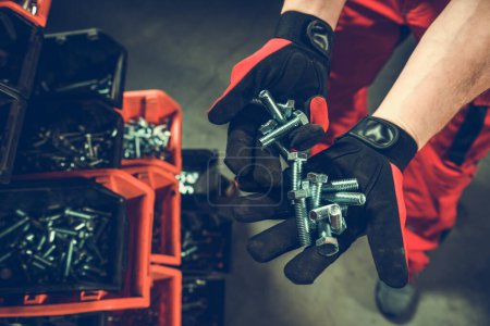 Foto de Trabajador con un montón de pernos metálicos en sus manos cubiertos por guantes protectores. - Imagen libre de derechos