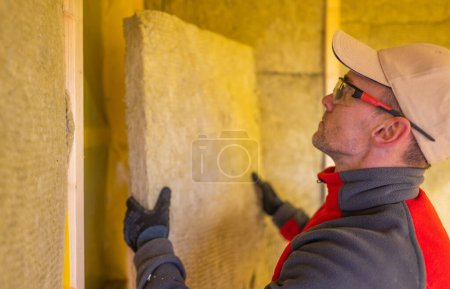 Foto de Contratista de aislamiento profesional caucásico en sus 40 años instalando lana mineral de alta temperatura dentro de las paredes de la casa. - Imagen libre de derechos