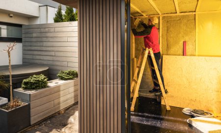 Photo for Caucasian Man in His 40s Insulating Newly Built Garden Shed with Mineral Wool. Walls Insulation Performed by General Contractor. - Royalty Free Image