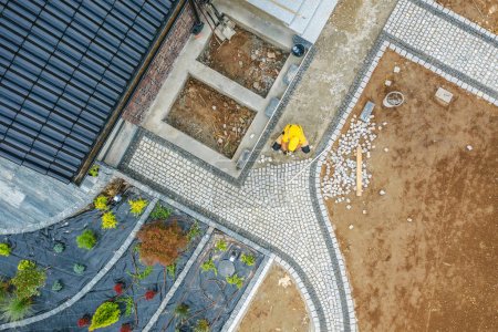 Photo for Creating New House Surrounding with Back Yard Garden. Worker Building Granite Bricks Paths. Aerial View. - Royalty Free Image