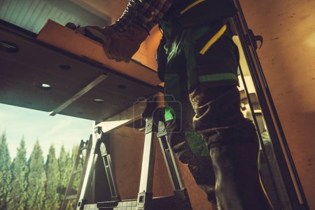 Téléchargez les photos : Vue du bas du menuisier professionnel coupant la planche en bois dans son atelier à l'aide de scie manuelle à bois. - en image libre de droit