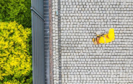 Foto de Vista aérea del trabajador de la construcción en traje de trabajo amarillo Acabado de pavimentar el camino de entrada en el patio delantero de la casa residencial. - Imagen libre de derechos