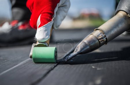 Photo for Roof Worker Attaching Pieces of EPDM Membrane Roofing Material Using Hot Air Blower and Industrial Roller. - Royalty Free Image