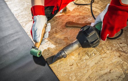 Photo for Caucasian Roofing Worker Installing EPDM Membrane Material Using Hot Air Blower and a Roller - Royalty Free Image