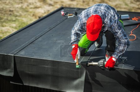 Téléchargez les photos : Installation de membranes EPDM au-dessus d'un abri de jardin. Travailleur professionnel attachant des morceaux de matériel utilisant le ventilateur. - en image libre de droit