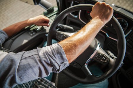 Truckers Hand on a Semi Truck Steering Wheel Close Up Photo. Caucasian Professional Driver Theme. Transportation Industry.