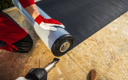 Photo for Roof Worker with Roll of EPDM Rubber Membrane Material Preparing to Cover Plywood Roof - Royalty Free Image