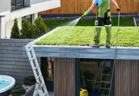 Caucasian Landscaper Watering Green Roof Sedum Plants Newly Installed on a Roof. Modern Landscaping Theme.