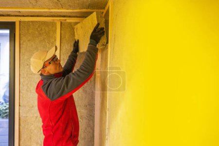 Photo for Caucasian Construction Worker Insulating Modern Garden Shed Using Mineral Wool. - Royalty Free Image