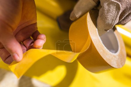 Photo for Closeup of Yellow Industrial Masking Tape in Hands of Professional Contractor. Construction Tools and Equipment. - Royalty Free Image