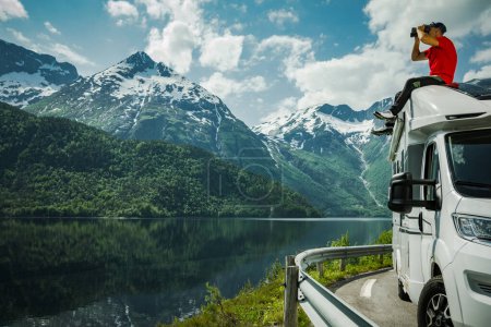 Foto de Hombre explorando paisaje escénico noruego usando prismáticos mientras está sentado en su techo autocaravana RV - Imagen libre de derechos