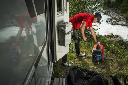 Homme caucasien tirant vers le haut générateur d'inverseur portable alimenté au gaz pour brancher son camping-car pendant hors grille Wild Camping.