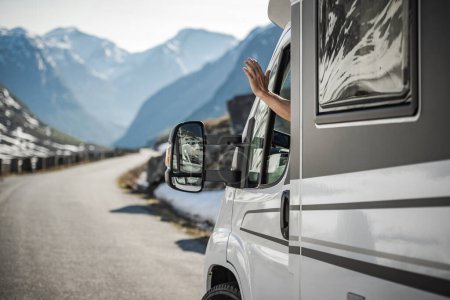 Kaukasischer Kastenwagenfahrer, der freundliche Handgesten macht, während er durch die malerische Landschaft reist. Lebensthema Van.