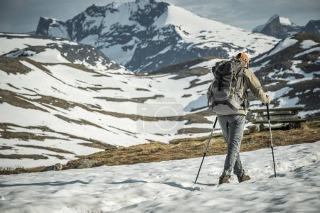 Foto de Atrás Vista del turista equipado profesionalmente con mochila y postes de trekking Senderismo en las montañas nevadas noruegas. Tema de actividades recreativas al aire libre. - Imagen libre de derechos
