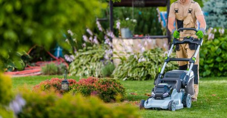 Photo for Gardener Taking Care of a Lawn. Trimming Grass Using Electric Mower - Royalty Free Image