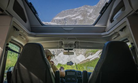 Photo for Caucasian Tourist Inside a Modern Camper Van RV with Panoramic Windows. Staying in Front of a Glacier - Royalty Free Image