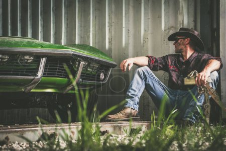 Foto de Cowboy americano caucásico sentado junto a su almacenamiento con su coche clásico - Imagen libre de derechos