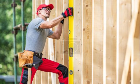 Téléchargez les photos : Entrepreneur de construction caucasien avec un instrument de niveau Esprit dans sa main mesurant les niveaux verticaux. - en image libre de droit