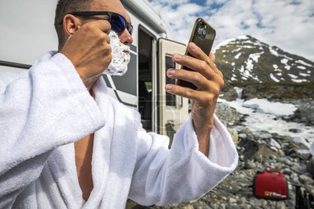 Photo for Caucasian Tourist Shaving His Face in Front of His RV Camper Van Using Smartphone Camera as Mirror - Royalty Free Image